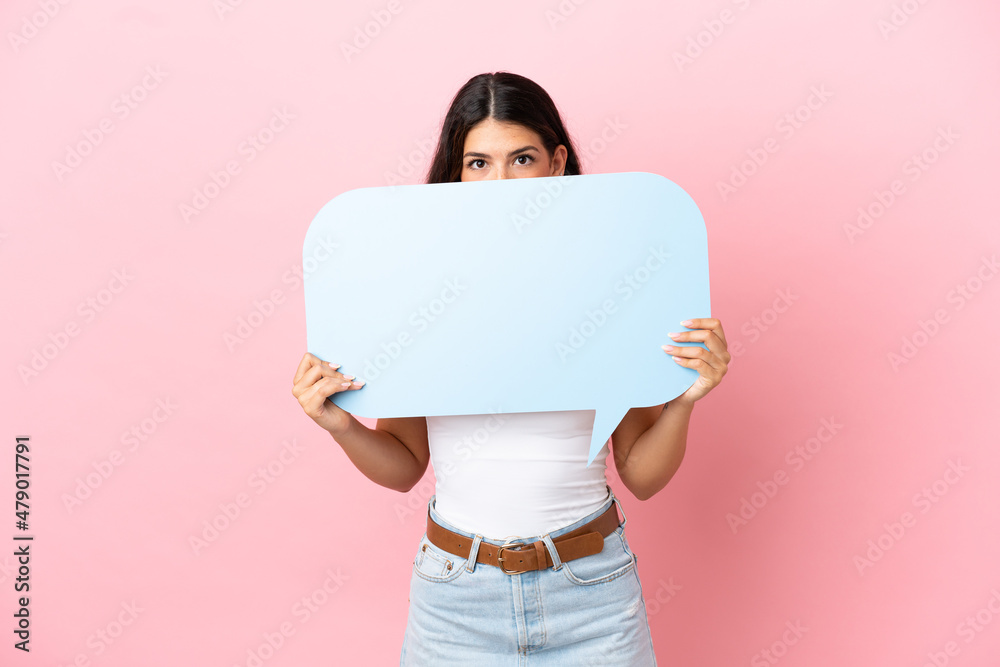 Young caucasian woman isolated on pink background holding an empty speech bubble hiding behind it hiding behind it Young caucasian woman isolated on pink background holding an empty speech bubble hiding behind it hiding behind it