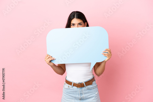 Young caucasian woman isolated on pink background holding an empty speech bubble hiding behind it hiding behind it