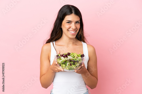 Young caucasian woman isolated on pink background holding a bowl of salad with happy expression