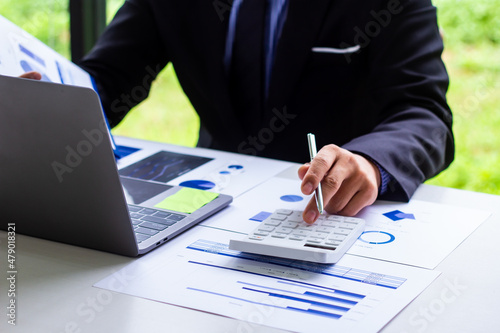 Male finance worker calculates last quarter's earnings figures and points to documents to present, business man checks company income and finance documents, modern business man concept.