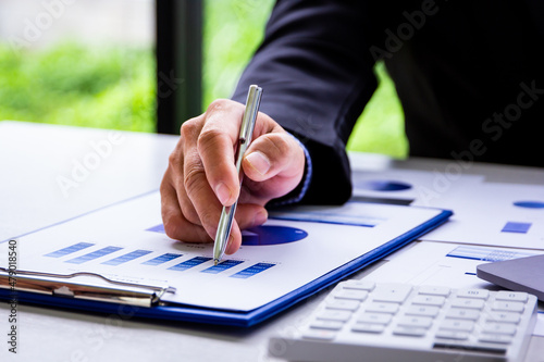 Male accountant calculates last quarter's earnings figures and points to documents to present, business man checking company income and finance documents, modern business man concept.