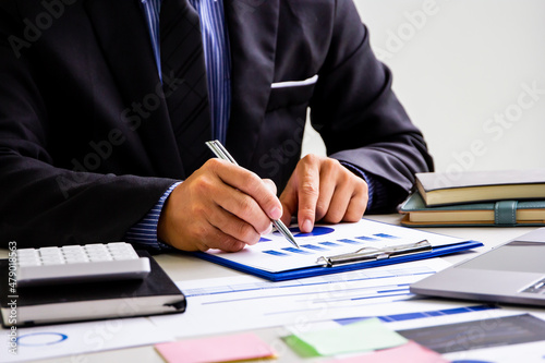 Male finance worker calculates last quarter's earnings figures and points to documents to present, business man checks company income and finance documents, modern business man concept.