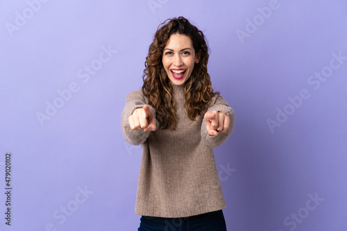 Young caucasian woman isolated on purple background surprised and pointing front © luismolinero