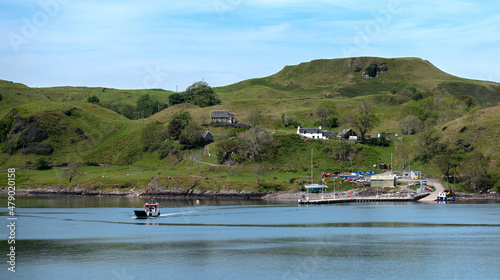 Small ferry returns from rural Scottish island with passengers and supplies - sunshine and summer conditions - blue water.
