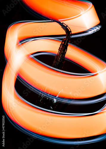 Saxophone instrument wrapped in vibrant light ribbons (orange and white) - light trail photography using brass instruments as the subject.