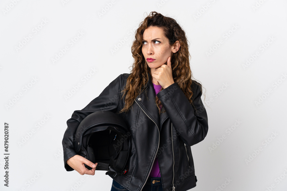 Young caucasian woman holding a motorcycle helmet having doubts and thinking