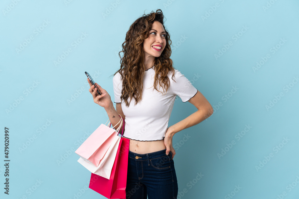 Young caucasian woman isolated on blue background holding shopping bags and a mobile phone Young caucasian woman isolated on blue background holding shopping bags and a mobile phone