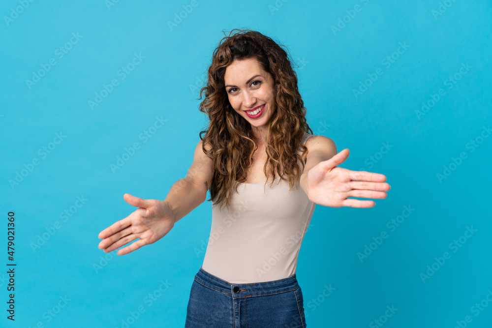 Fototapeta premium Young caucasian woman isolated on blue background presenting and inviting to come with hand