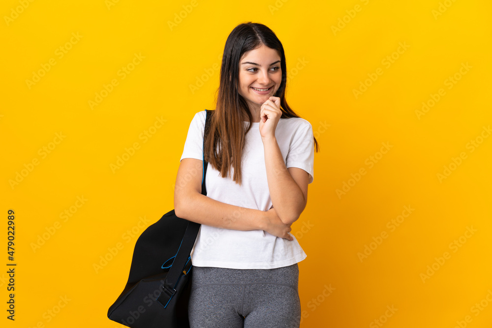 Young sport woman with sport bag isolated on yellow background thinking an idea while looking up