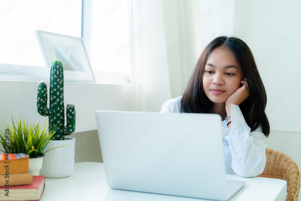 Portrait Cute Asian teen with long hair Wearing a white shirt, sitting online studying with a laptop on the bedroom table with a thoughtful face. Portrait Cute Asian teen with long hair Wearing a white shirt, sitting online studying with a laptop on the bedroom table with a thoughtful face.