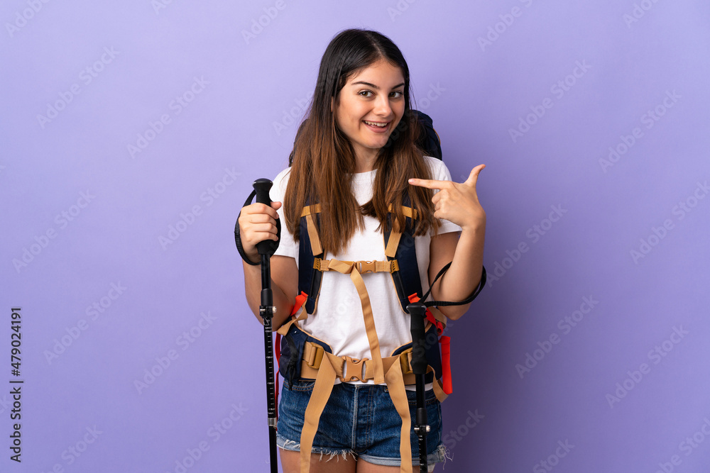 Young woman with backpack and trekking poles isolated on purple background giving a thumbs up gesture