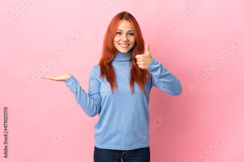 Teenager Russian girl isolated on pink background holding copyspace imaginary on the palm to insert an ad and with thumbs up