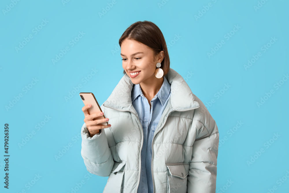 Pretty young woman in stylish warm clothes and with phone on color background Pretty young woman in stylish warm clothes and with phone on color background