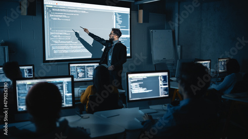 Teacher Giving Computer Science Lecture to Diverse Multiethnic Group of Female and Male Students in Dark College Room. Projecting Slideshow with Programming Code. Explaining Information Technology. photo