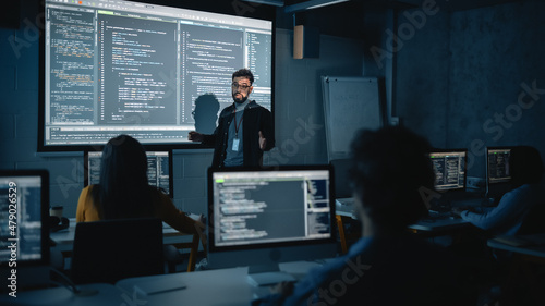 Teacher Giving Computer Science Lecture to Diverse Multiethnic Group of Female and Male Students in Dark College Room. Projecting Slideshow with Programming Code. Explaining Information Technology.