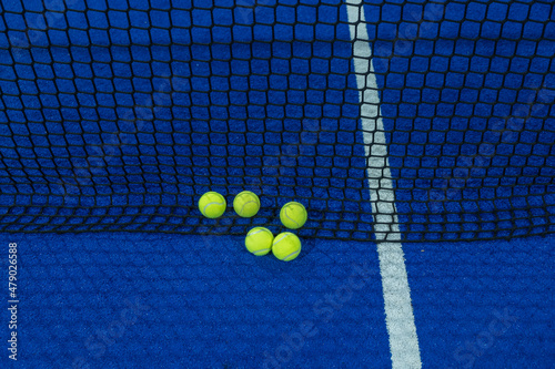 Multiple balls in the net of a blue paddle tennis court. © Vic