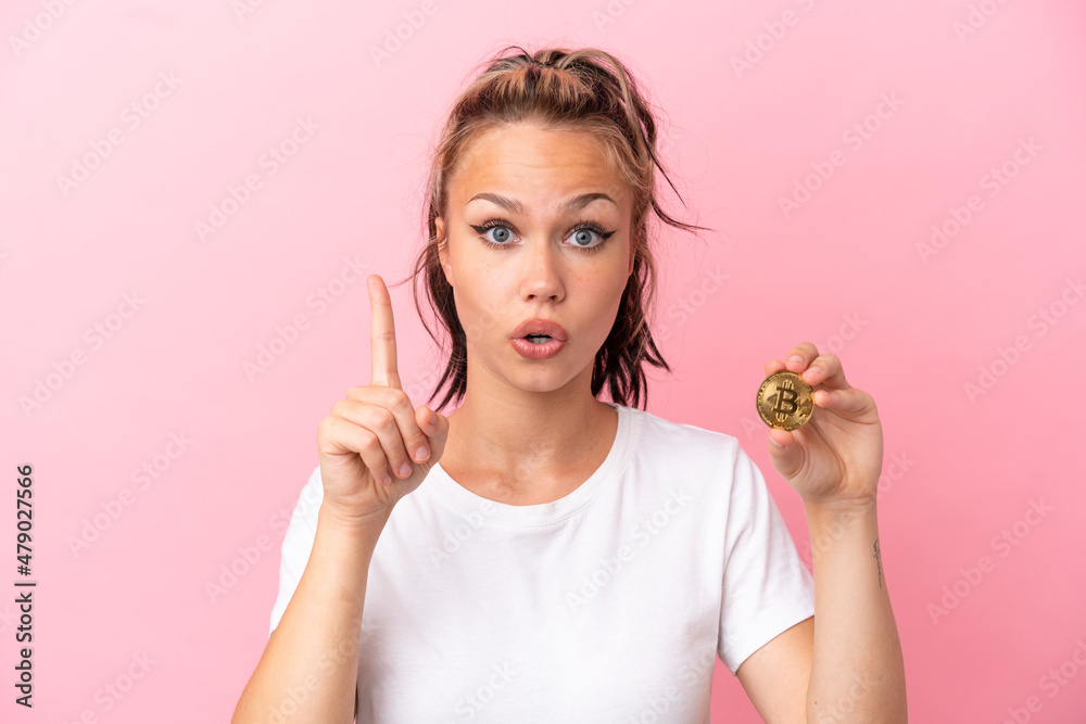 Teenager Russian girl holding a Bitcoin isolated on pink background intending to realizes the solution while lifting a finger up