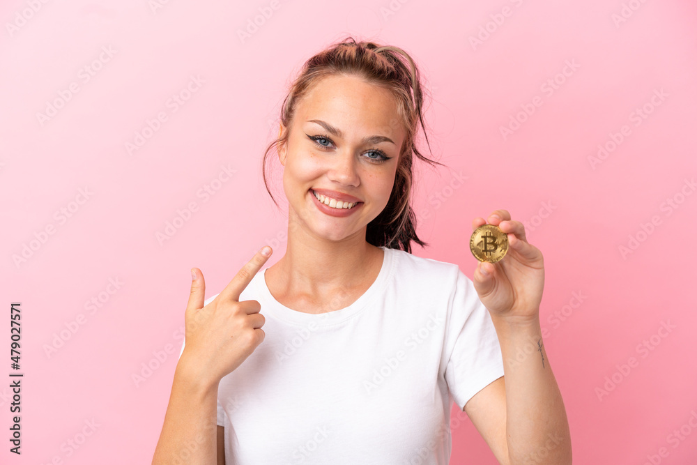 Teenager Russian girl holding a Bitcoin isolated on pink background giving a thumbs up gesture Teenager Russian girl holding a Bitcoin isolated on pink background giving a thumbs up gesture