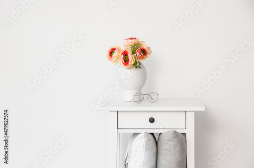 White bedside table with flowers in vase and pillows on shelf near light wall