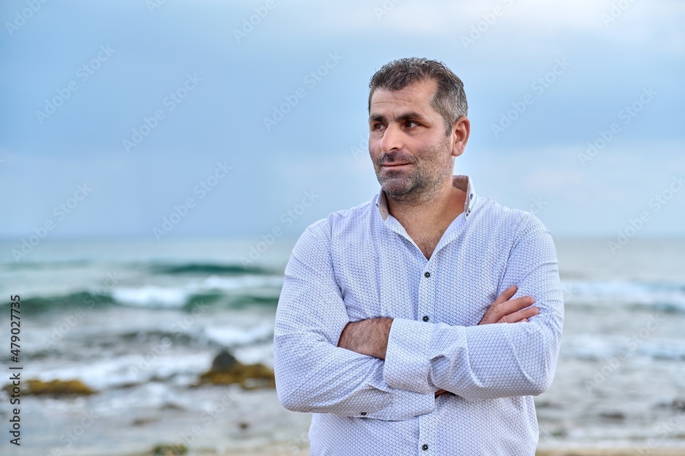 Portrait of confident mature man with crossed arms, sky sea background, copy space.