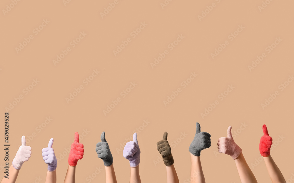 Women in warm gloves showing thumb-up gesture on beige background Women in warm gloves showing thumb-up gesture on beige background