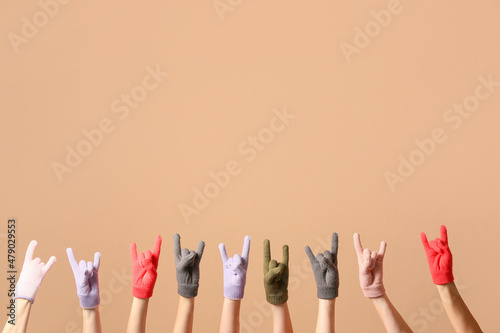 Women in warm gloves showing "devil horns" gesture on beige background