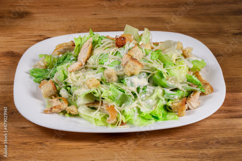 fresh caesar salad with chicken pieces served on white dish on wooden background