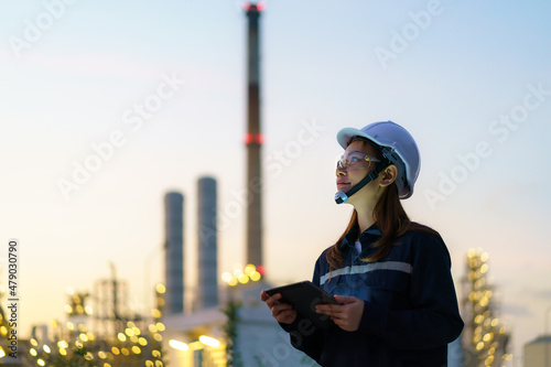 Asian woman petrochemical engineer working at night with digital tablet Inside oil and gas refinery plant industry factory at night for inspector safety quality control.