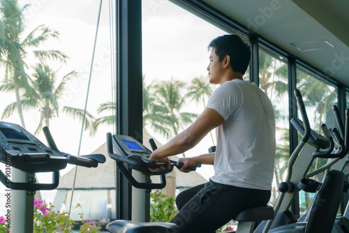 Asian man working out on indoor cycling at a resort fitness center in the morning.. © ake1150