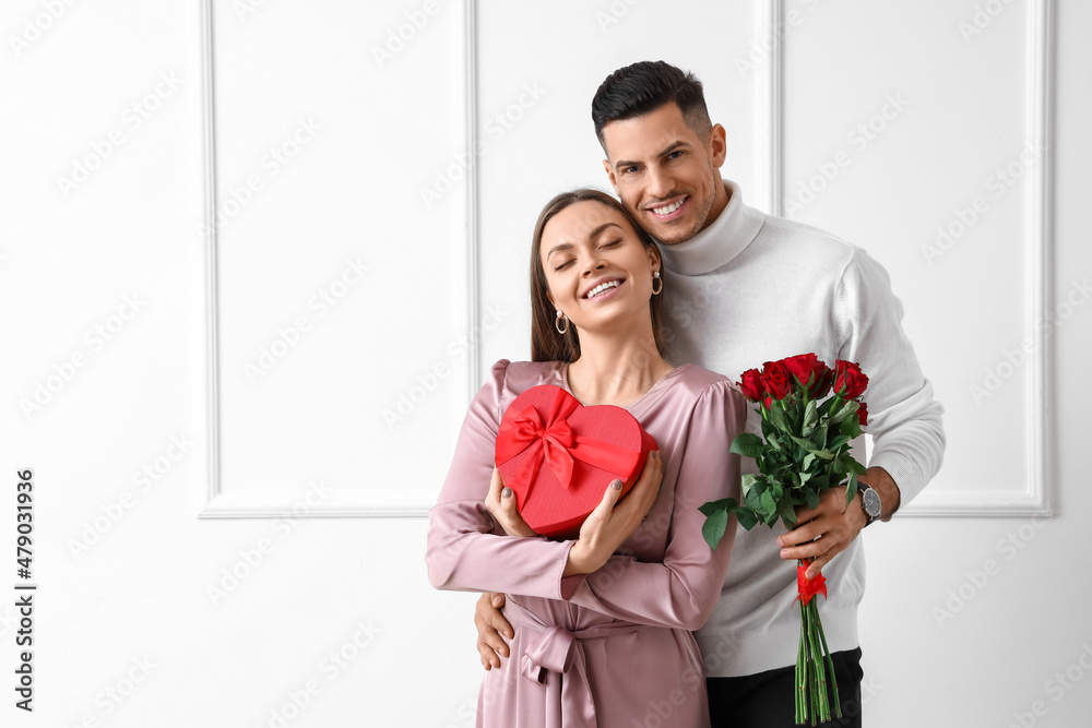 Happy young couple with gift and flowers on light background. Valentine's Day celebration Happy young couple with gift and flowers on light background. Valentine's Day celebration
