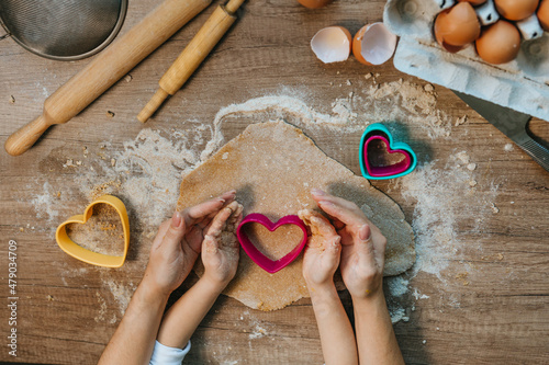 Top view of little girl with parent cutting heart shape cookies from rye dough photo