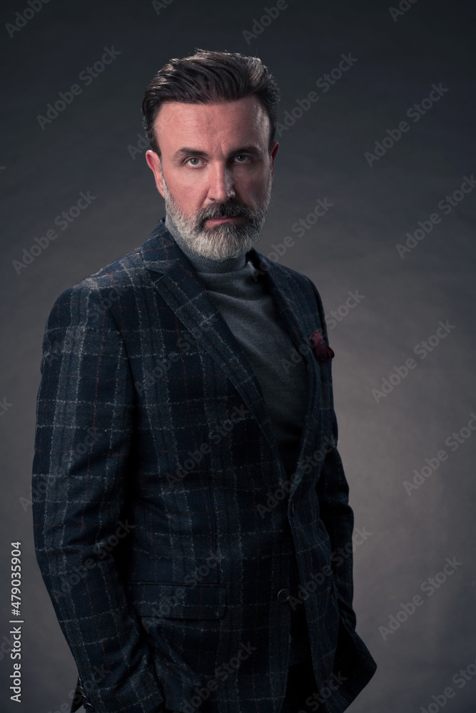 Obraz premium Portrait of a stylish elegant senior businessman with a beard and casual business clothes in photo studio isolated on dark background gesturing with hands