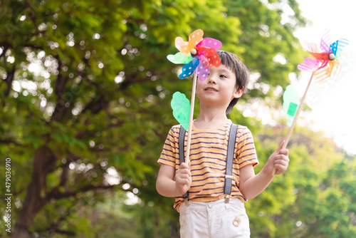 Boy playing with windmill, running, jumping in the park on summer vacation concept for freedom or the environment