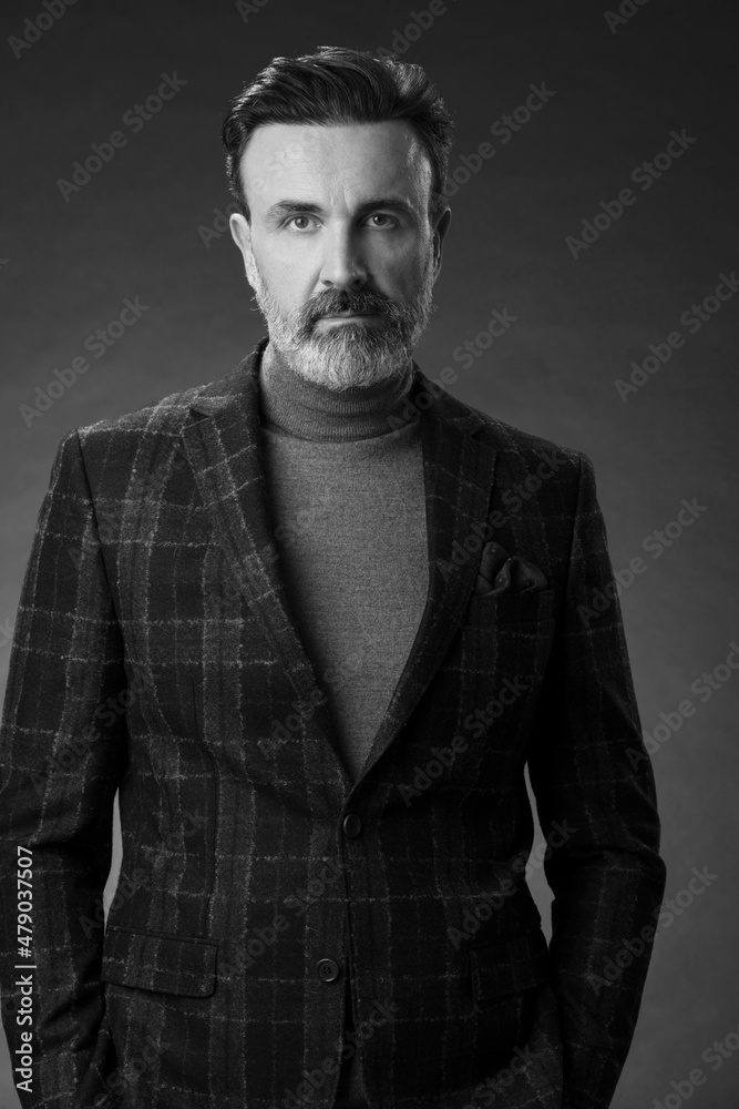 Obraz premium Portrait of a stylish elegant senior businessman with a beard and casual business clothes in photo studio isolated on dark background gesturing with hands