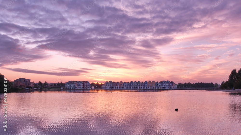 Purple skies and sunset over lake De Rietplas in Houten in the Netherlands. Row of colourful wooden newly built Dutch houses in the distance.