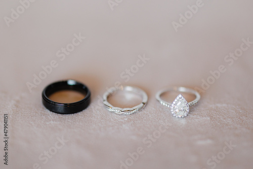 Three wedding rings on the white table One black groom's wedding ring, engagement and diamond wedding ring of the bride Close up 