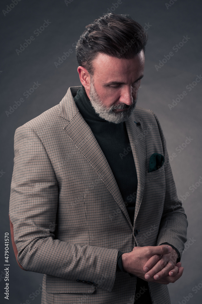 Fototapeta premium Portrait of a stylish elegant senior businessman with a beard and casual business clothes in photo studio isolated on dark background gesturing with hands