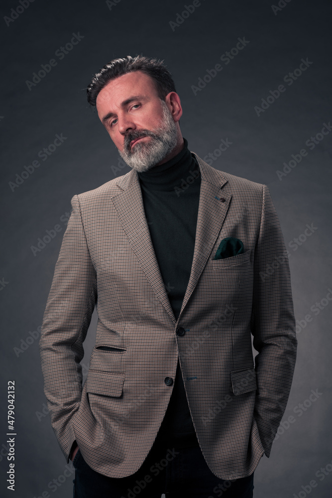 Portrait of a stylish elegant senior businessman with a beard and casual business clothes in photo studio isolated on dark background gesturing with hands
