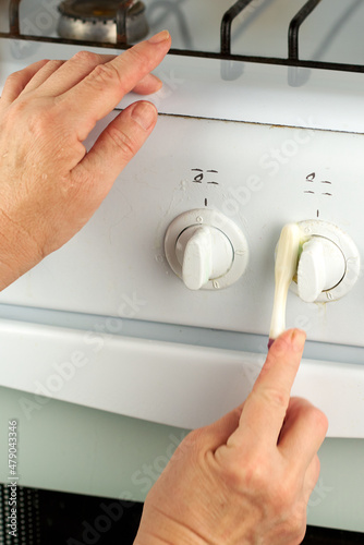 Female hands wash the taps of the white gas stove with a toothbrush. An unusual way of home cleaning