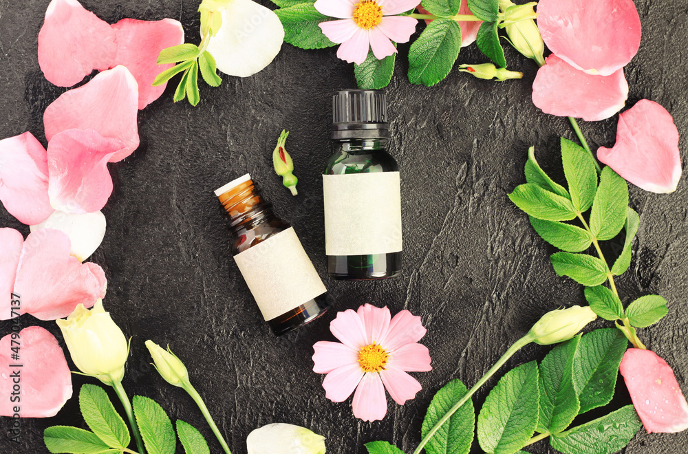 Φωτογραφία Herbal aromatherapy extract floral essential oil in bottles among bright flowers of wild rose pink petals and green leaves, top view black background