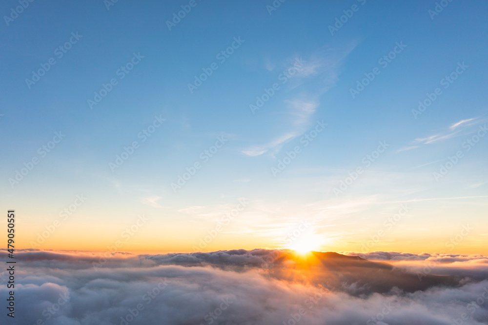 Sun shining above layer of white fluffy clouds at sunset