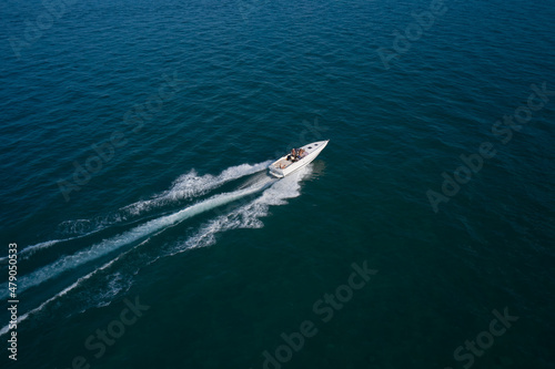 Boat on the water top view. White boat with people on dark blue water aerial view. People in a boat in motion top view.