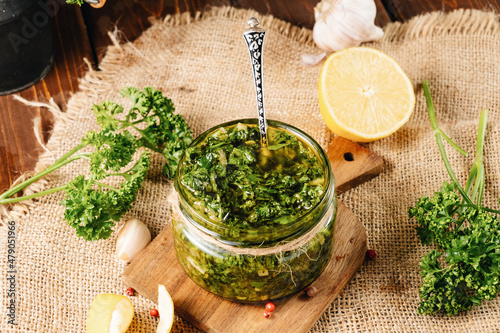 Jar of healthy green parsley-based chimichurri sauce. Wooden table with cloth. photo