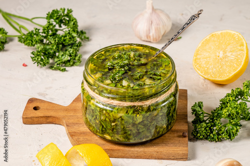 Green chimichurri sauce on a background of parsley, lemon, white table. photo