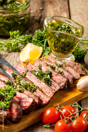 Sliced beef steak grilled and served on a wooden board with homemade chimichurri sauce.