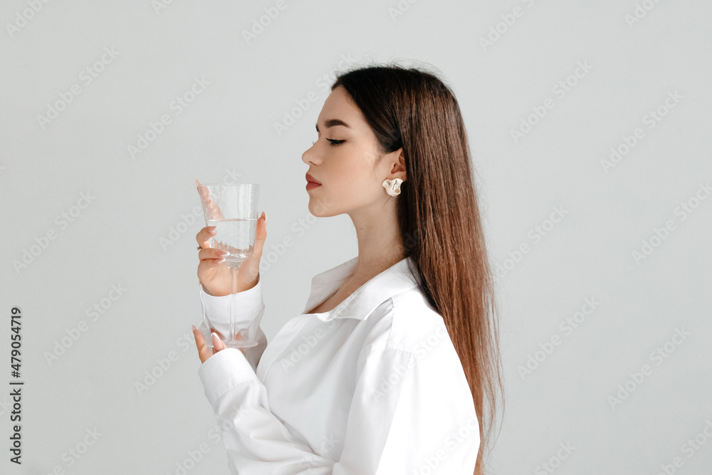 Profile of a young woman with perfect makeup and strait dark hair, holding glass of water, studio portrait on white. Profile of a young woman with perfect makeup and strait dark hair, holding glass of water, studio portrait on white.