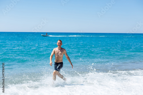 Attractive young man with a beautiful body in shorts walks along the sandy seashore and enjoying summer vacation