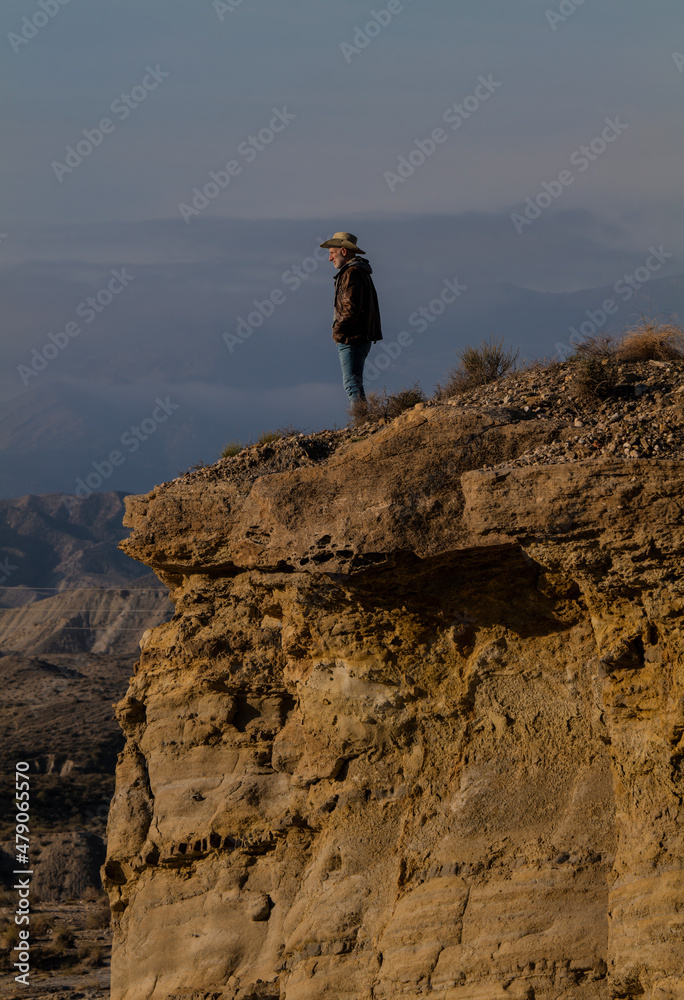 Adult man in cowboy hat standing on top of cliff in Tabernas Desert, Almeria, Spain