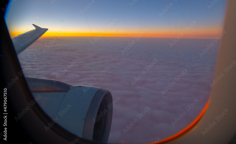Fototapeta premium view of sea of clouds at sunset out of airplane window seat window orange sunset with pink and purple fluffy clouds as seen while in flight on airplane our of plane window heavenly horizontal format 