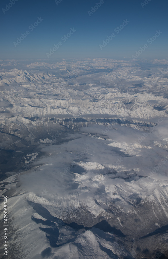 Aerial view of snow covered rocky mountains in Canada or Canadian Rockies as seen from window seat of airplane while in flight travelling on plane from Alberta, Canada to British Columbia 
